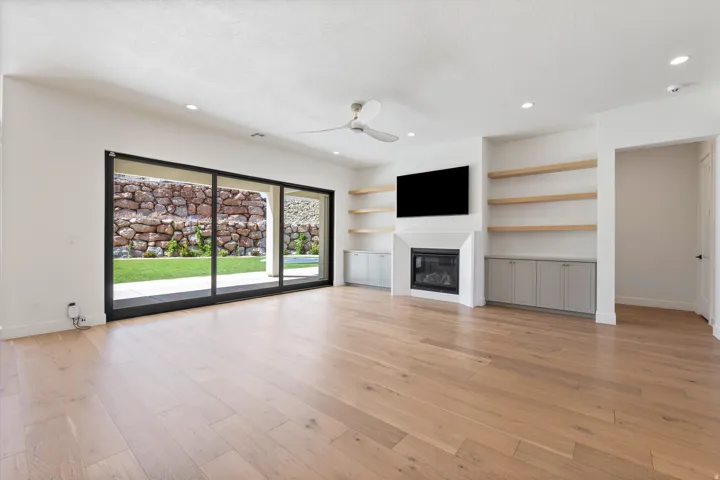Expansive living space featuring wood-finish flooring, a linear fireplace, built-in shelving, recessed lighting, and a large sliding glass door