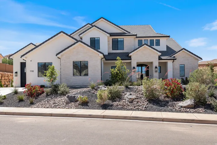Contemporary stucco exterior with stone accents, dark-framed windows, a prominent arched entry, and a dark tile roof