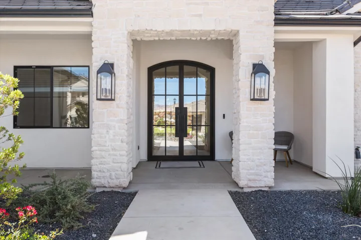 Stone facade entrance featuring a double arched iron door, exterior sconces, and a concrete pathway