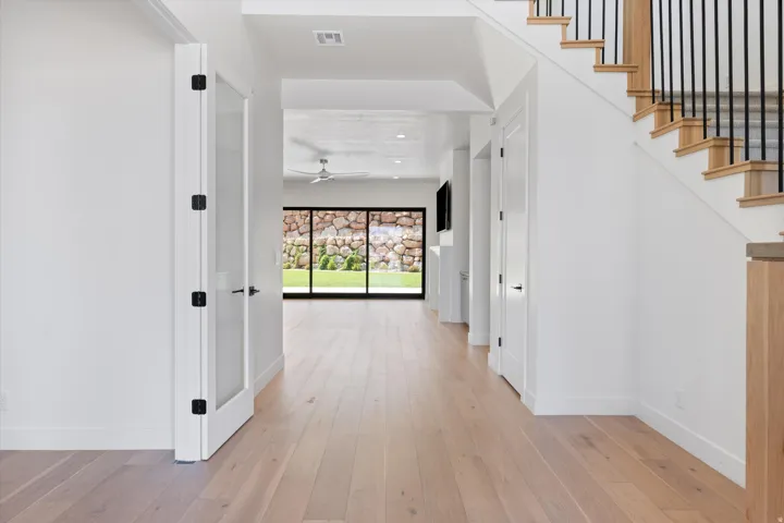 Light wood-finish flooring extending through an open hall, white walls, and a staircase with black metal balusters