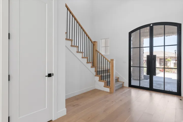 Arched double entry doors with black framing, wood-finish flooring, staircase with wood newel posts and railings, and white panel doors