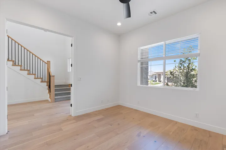 Recessed lighting, wood-finish flooring, staircase with wood-finish handrail and black metal spindles, ceiling fan, and large window with blinds