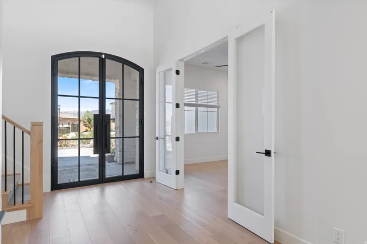Arched black-frame glass entry doors, wood-finish flooring, white walls, and a wood staircase with black metal balusters