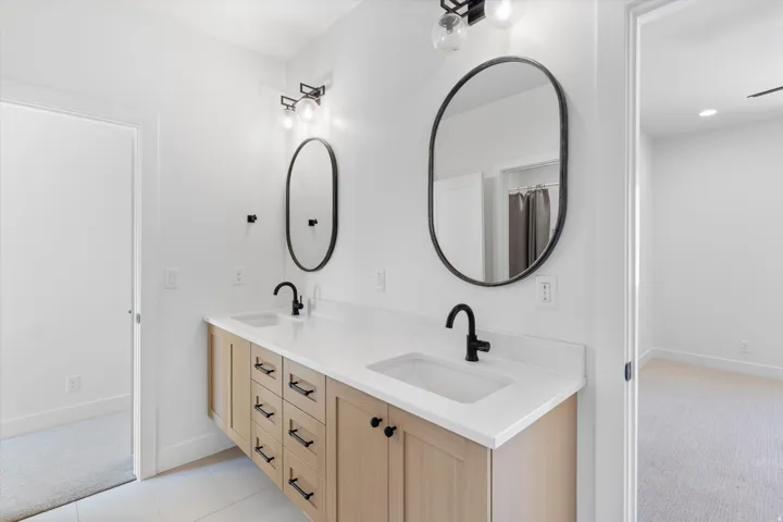 Double vanity with light wood-finish cabinetry, white countertops, and matte black fixtures