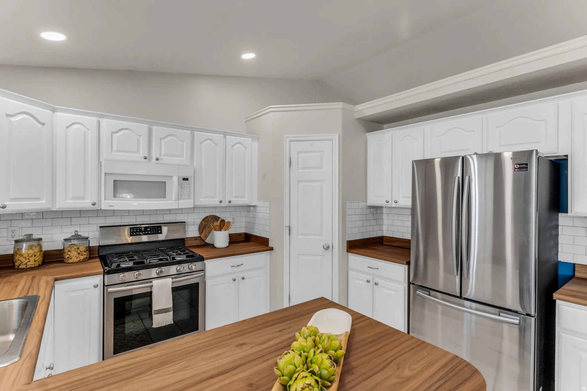 White cabinetry with silver hardware, wood-finish countertops, stainless steel appliances, subway tile backsplash, and recessed lighting