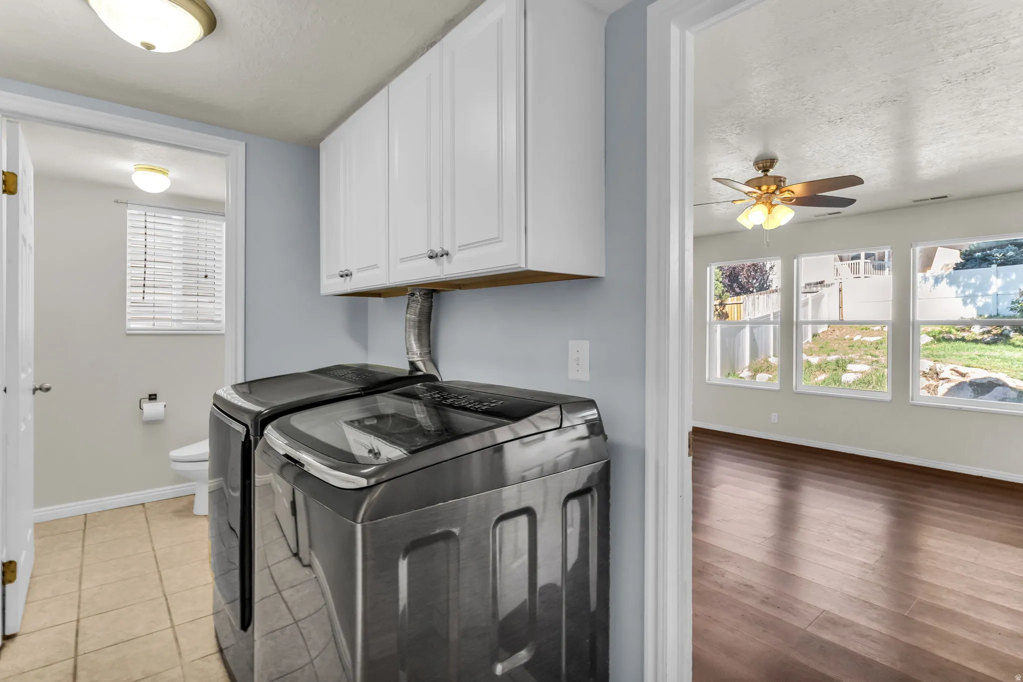 White cabinetry, stainless steel appliances, wood-finish flooring, ceiling fan with light fixture, and multiple windows