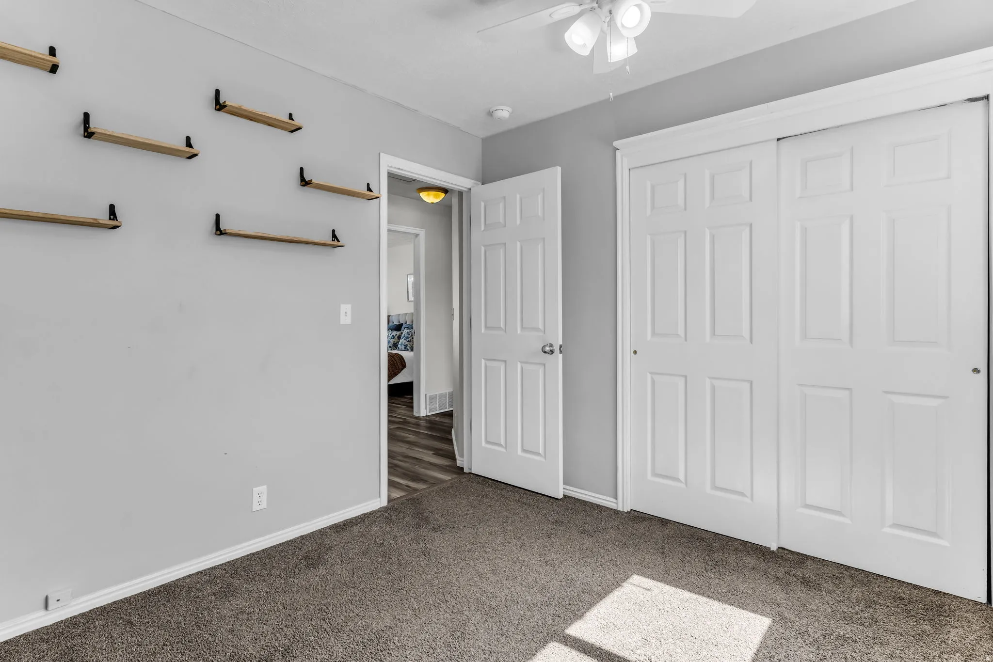 Plush carpeting, ceiling fan with light fixture, built-in shelving, white paneled doors, and a sliding closet