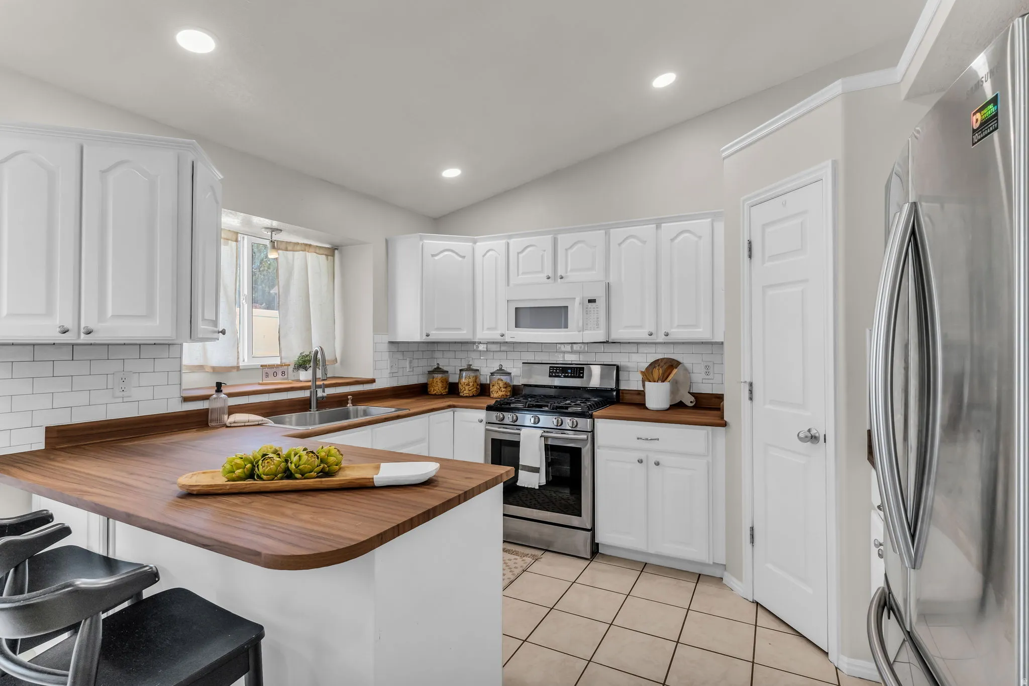 White cabinetry, wood-finish countertops, stainless steel appliances, subway tile backsplash, and tile flooring