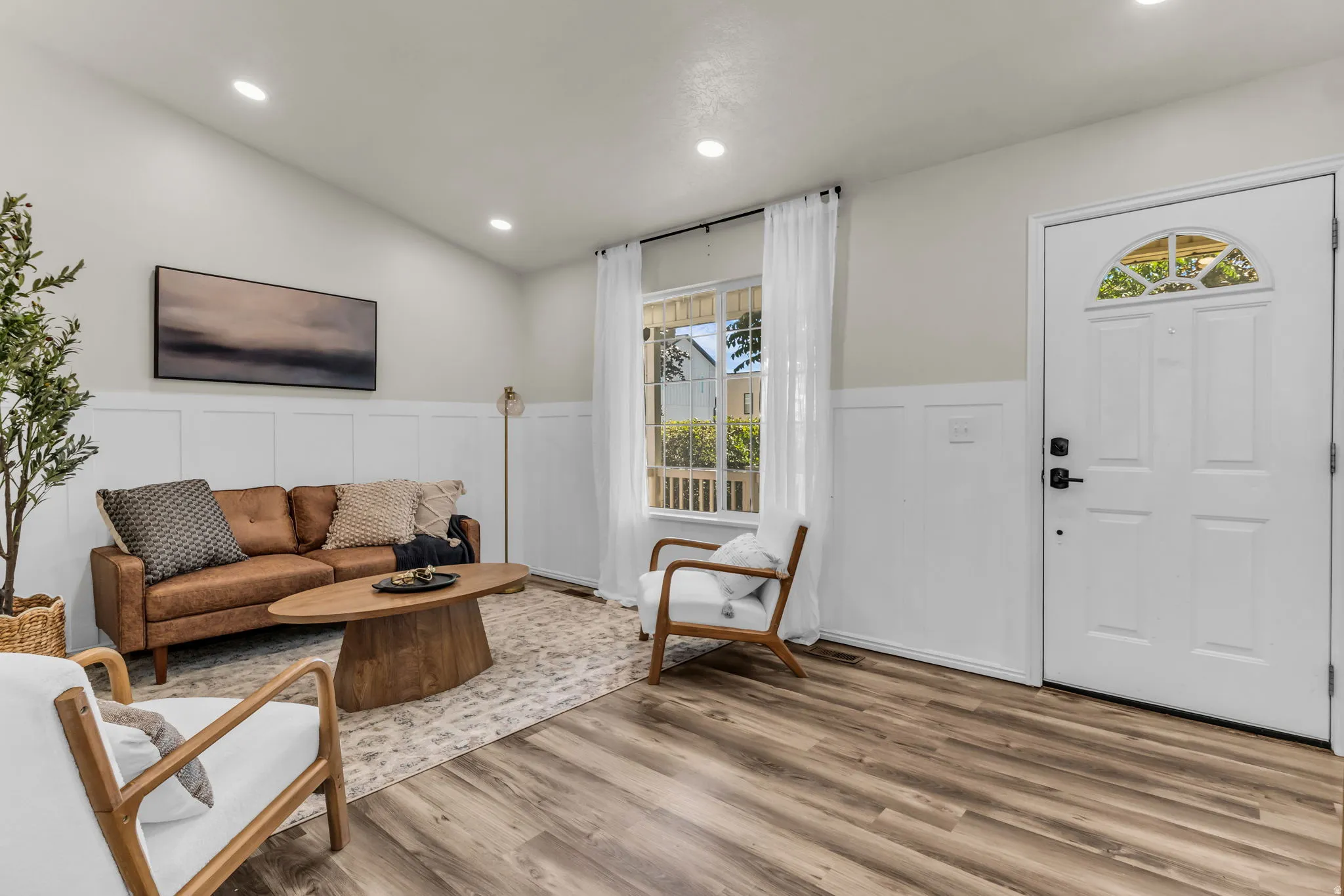 Wood-finish flooring, white paneled wainscoting, vaulted ceiling with recessed lighting, and a front entry door with an arched transom window