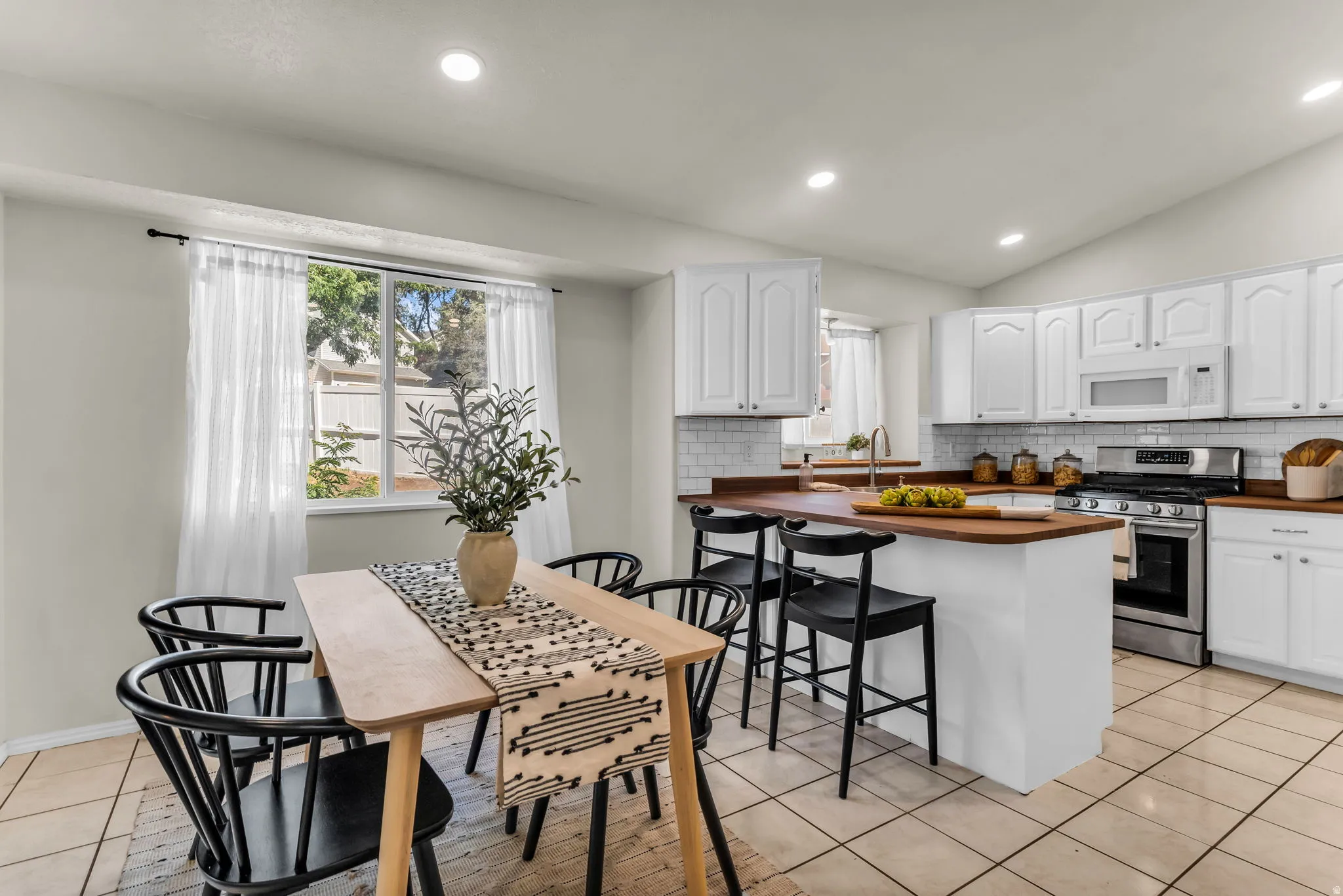 Kitchen featuring white cabinetry, subway tile backsplash, stainless steel appliances, wood-finish countertops, and tile flooring