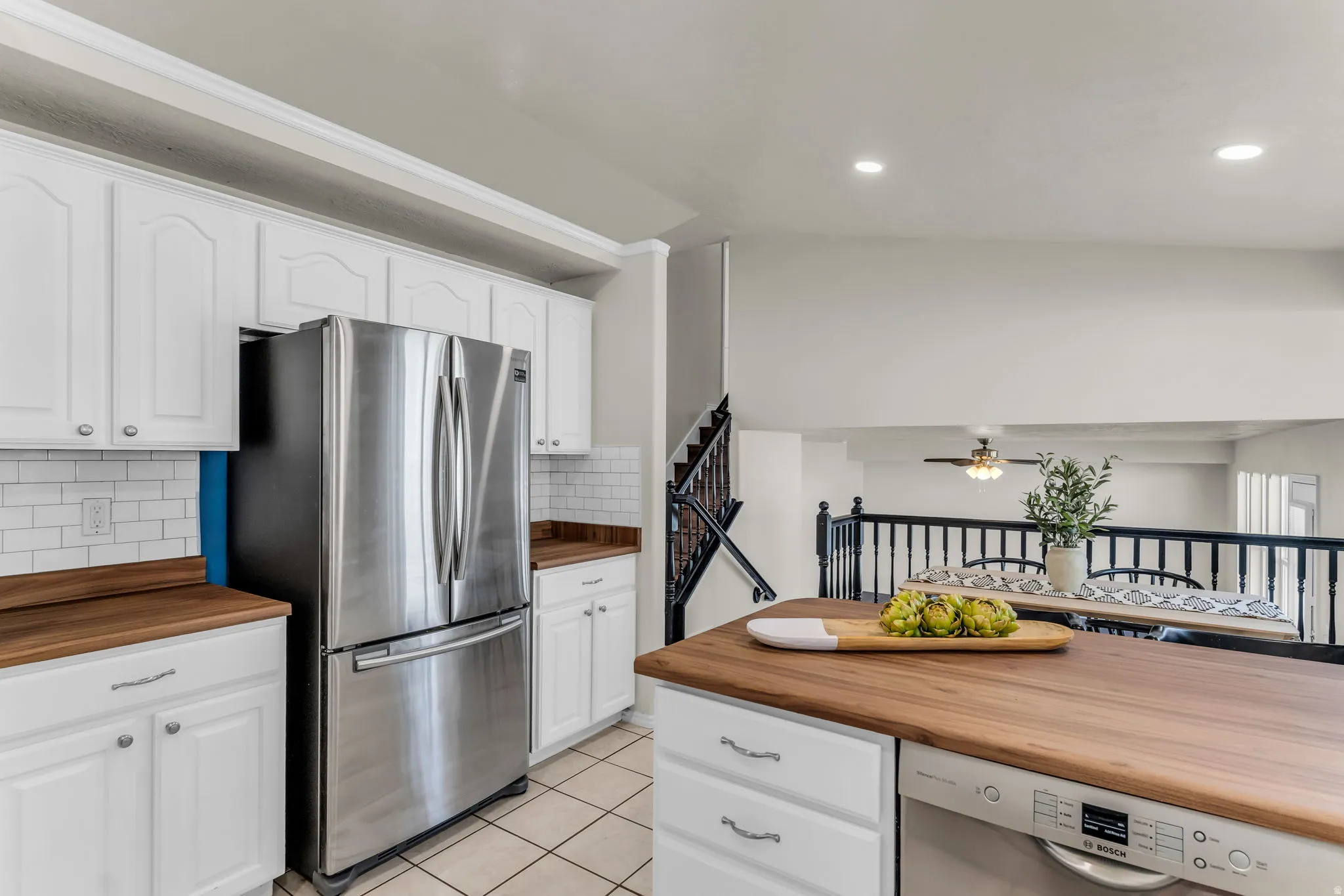 White cabinetry, wood-finish countertops, stainless steel appliances, white subway tile backsplash, and recessed lighting