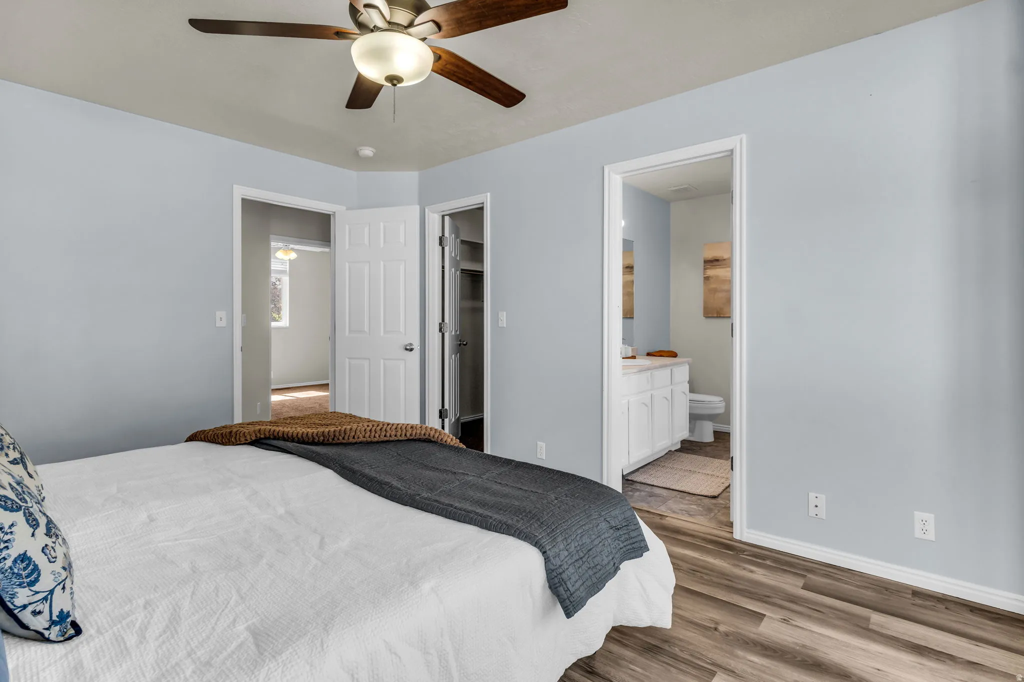 Wood-finish flooring, ceiling fan with integrated lighting, built-in closet shelving, white vanity with counter space, and a wall-mounted mirror