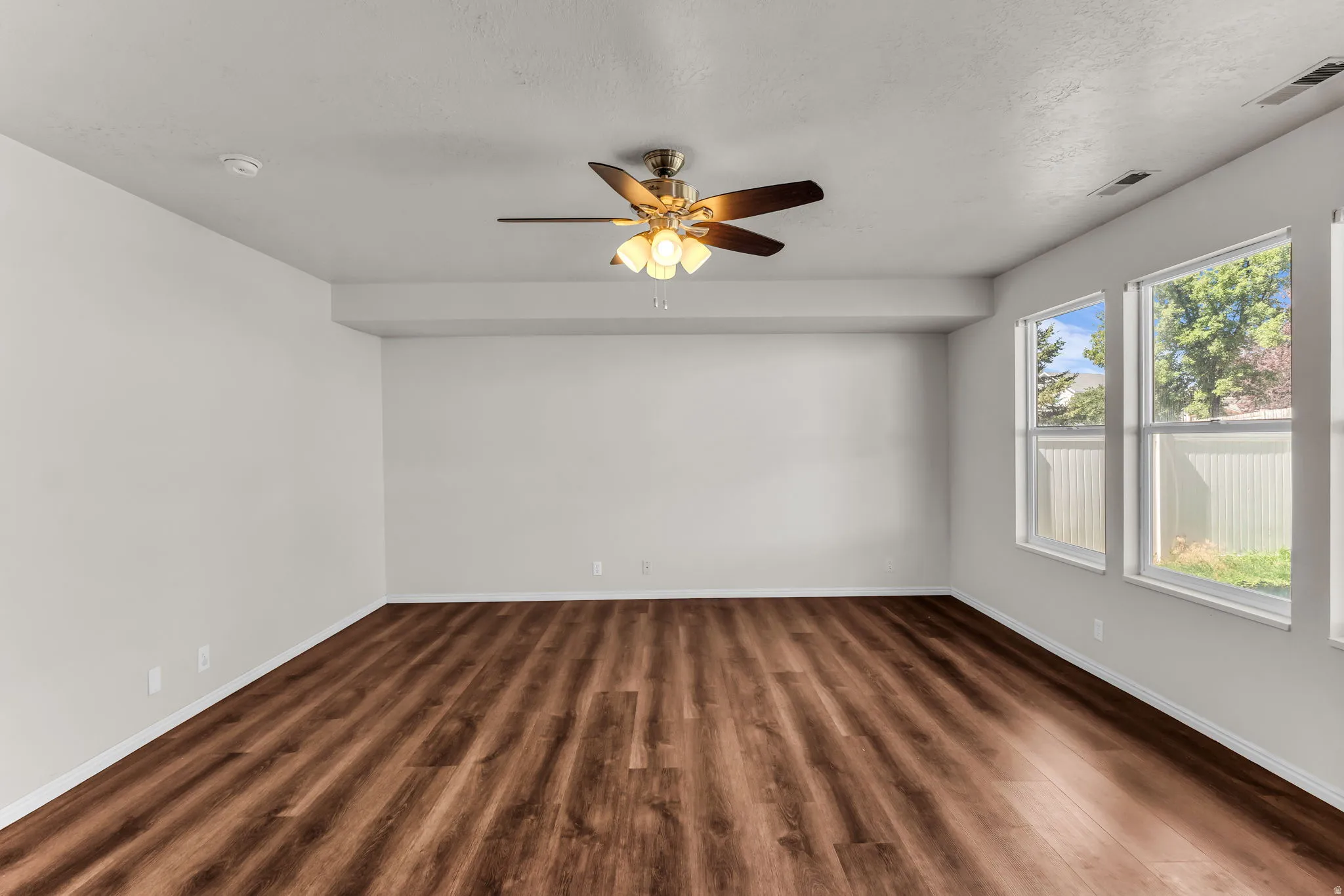 Spacious room featuring wood-finish flooring, a ceiling fan with integrated lighting, and multiple windows