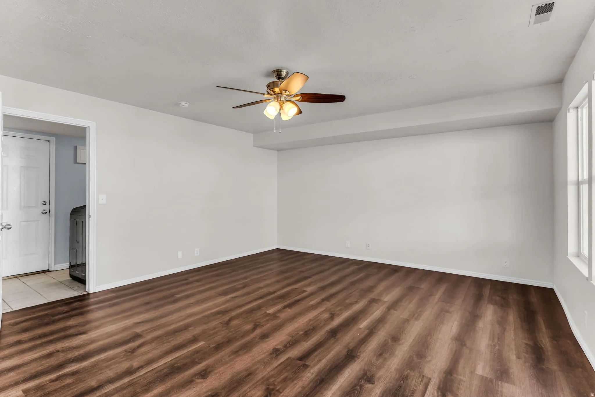 Spacious room featuring wood-finish flooring, a ceiling fan with integrated lighting, and multiple windows