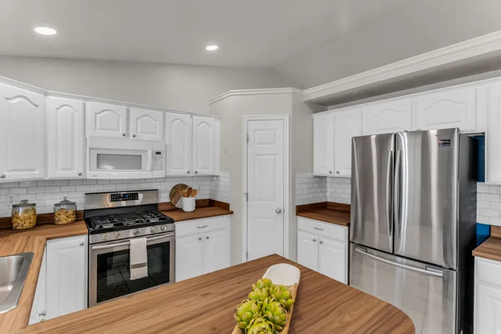 White cabinetry with silver hardware, wood-finish countertops, stainless steel appliances, subway tile backsplash, and recessed lighting
