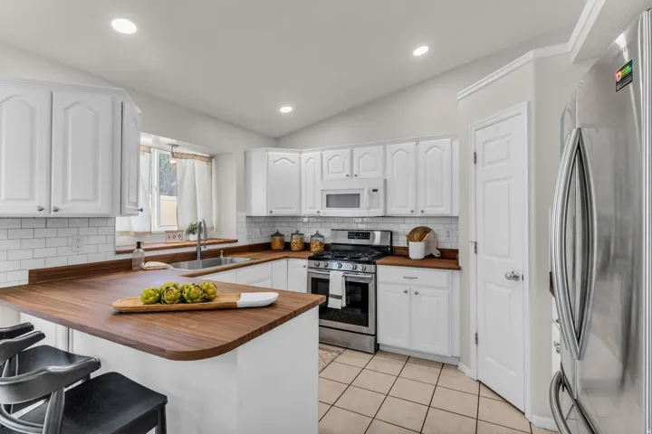 White cabinetry, wood-finish countertops, stainless steel appliances, subway tile backsplash, and tile flooring