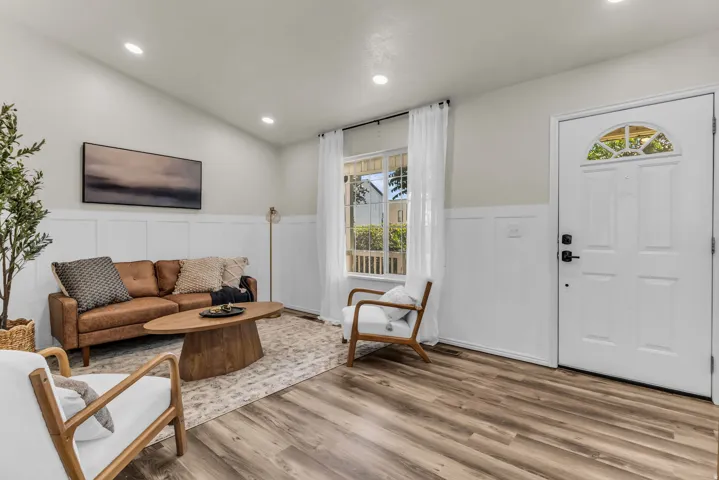 Wood-finish flooring, white paneled wainscoting, vaulted ceiling with recessed lighting, and a front entry door with an arched transom window
