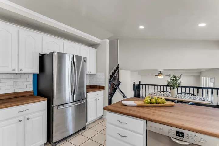 White cabinetry, wood-finish countertops, stainless steel appliances, white subway tile backsplash, and recessed lighting