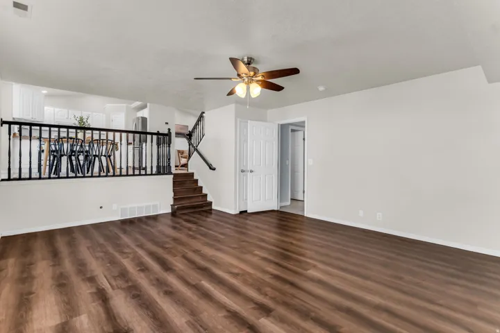 Spacious room with wood-finish flooring, white walls, and a ceiling fan