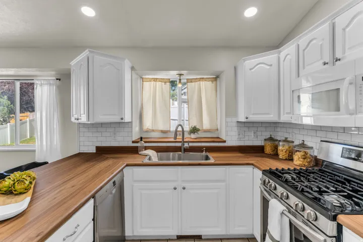 White cabinetry with silver-tone hardware, wood-finish countertops, subway tile backsplash, and stainless steel sink