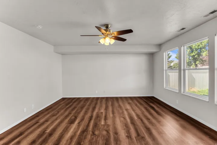 Spacious room featuring wood-finish flooring, a ceiling fan with integrated lighting, and multiple windows