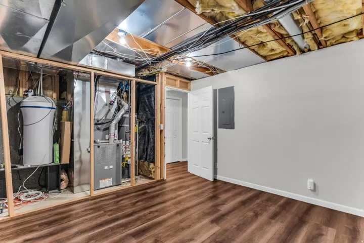 Finished flooring, exposed ceiling joists with insulation, internal structural framing, furnace, and water conditioning system