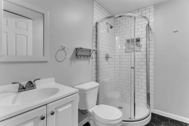 White subway tile shower with a curved glass enclosure, hexagonal floor tiling, a single vanity with storage, and a framed wall mirror