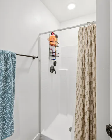 White shower stall with a dark bronze shower fixture and a recessed ceiling light