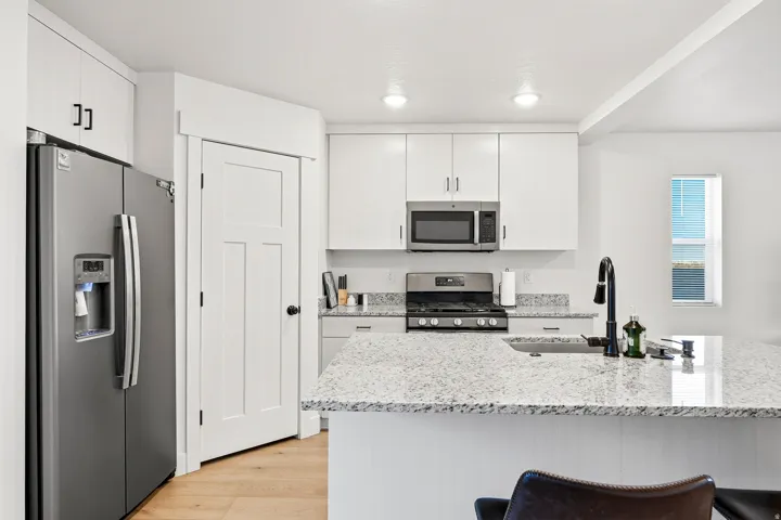 Stainless steel appliances, white cabinetry, integrated sink, light-toned countertops, and wood-finish flooring