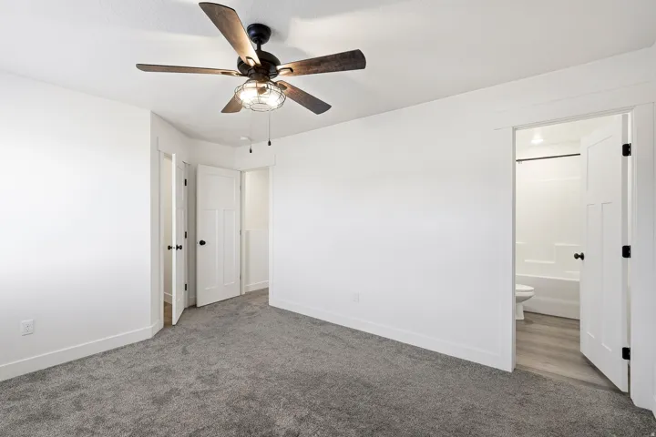 Carpet flooring, ceiling fan with integrated lighting, white interior doors, and a bathroom featuring a tub and toilet