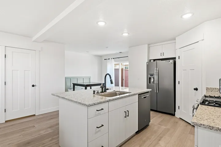 Kitchen featuring a center island with a stainless steel sink, granite countertops, wood-finish flooring, and recessed lighting