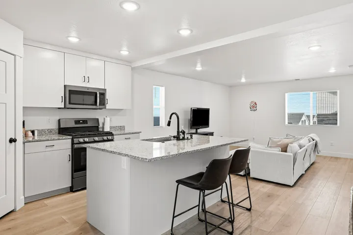 Kitchen featuring white cabinetry, stainless steel microwave, gas range, and a central island with a sink and granite-style countertop