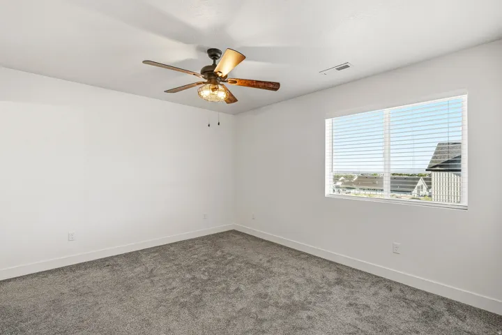 Bright room with a large window, neutral gray carpeting, white walls, and a ceiling fan with integrated lighting