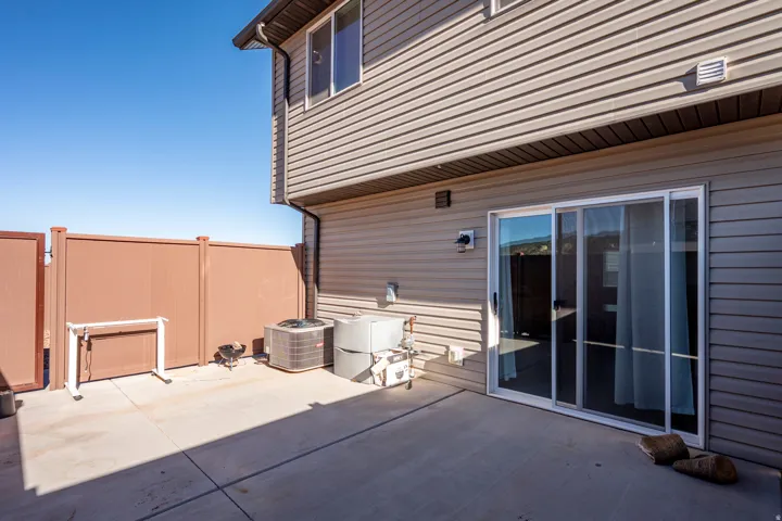 Concrete patio with a brown privacy fence, tan siding, and a white-framed sliding glass door