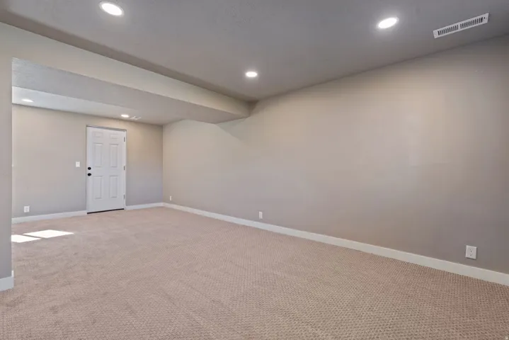 Recessed lighting illuminates neutral carpeting and light gray walls