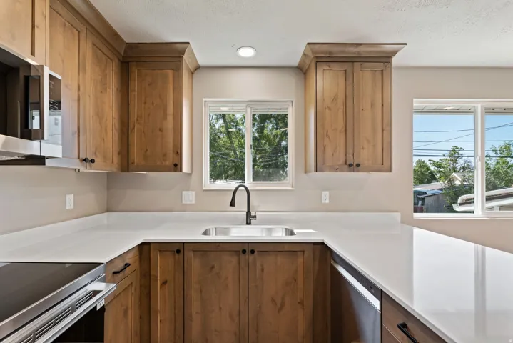 U-shaped kitchen with wood-finish cabinetry, light-toned countertops, stainless steel sink with matte black faucet, and an integrated electric range
