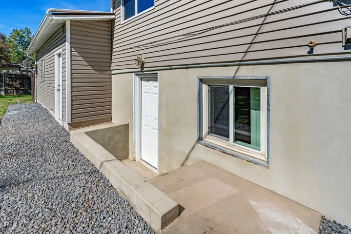 Cement foundation with a window well, concrete patio, and a side entry door