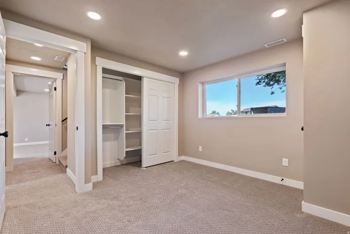 Neutral-toned carpeting in a room featuring a window, recessed lighting, and a closet with bifold doors and built-in shelving