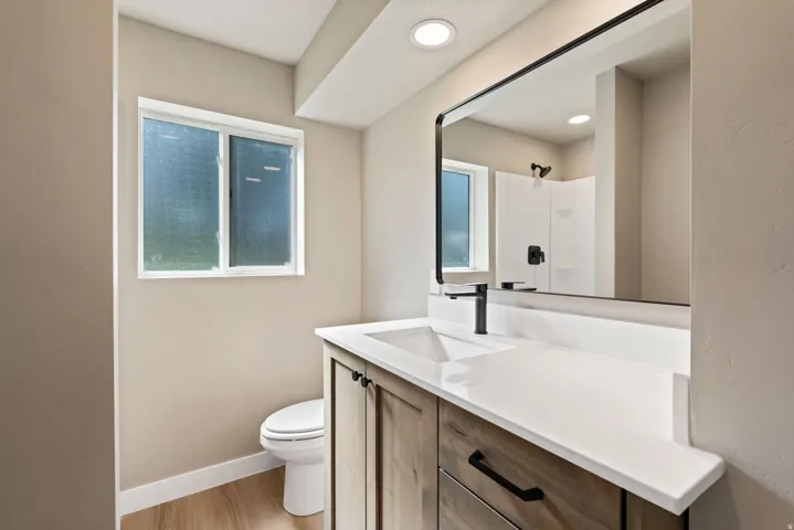 Contemporary bathroom featuring a wood-finish vanity with a white countertop, undermount sink, and black fixtures