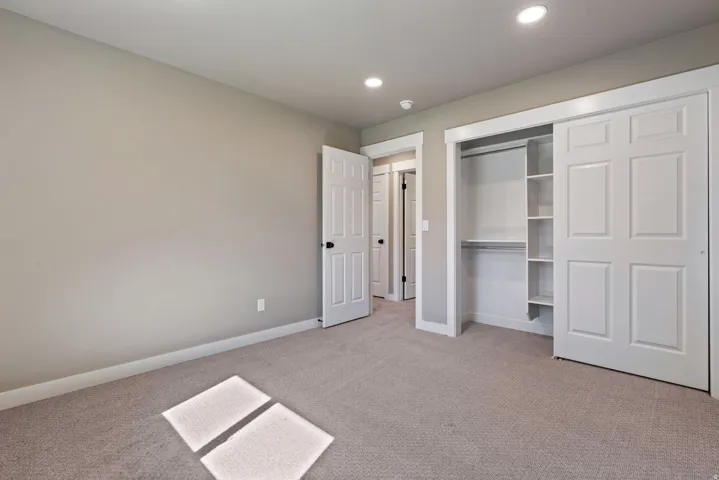 Recessed lighting, neutral wall paint, carpet flooring, a closet with sliding doors, and built-in shelving