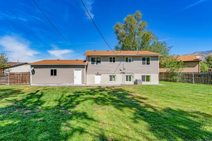Expansive green lawn, multi-level exterior, concrete patio, multiple windows, and a brown shingle roof
