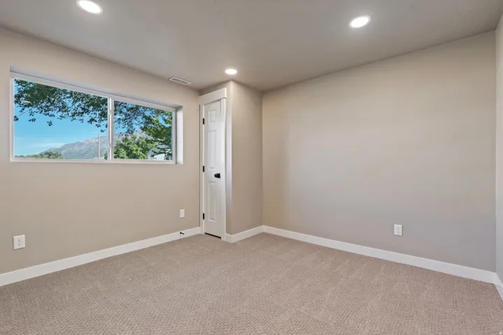 Recessed lighting, neutral wall paint, carpeted flooring, white trim, and a horizontal window with mountain scenery
