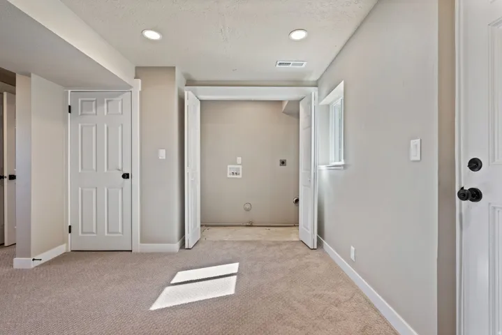 Recessed lighting, wall-to-wall carpeting, window with white trim, white paneled doors with black hardware, and an in-unit utility area