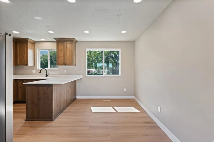 Wood-finish flooring, recessed lighting, wood cabinetry, light-toned countertops, and a kitchen island with seating capacity