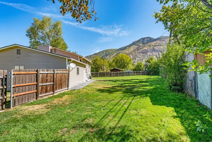 Expansive grassy yard area with a wood privacy fence and chain-link fencing, featuring a partial view of a mountain backdrop