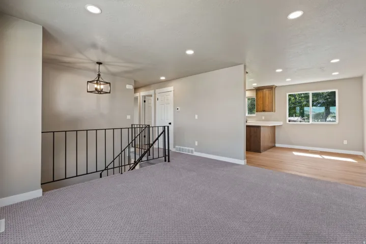 Recessed ceiling lighting, updated carpet, wood-finish flooring, black metal stair railing, and a modern chandelier