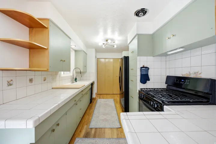 Kitchen featuring white tile countertops, light green cabinetry, a black gas range, and wood-finish flooring