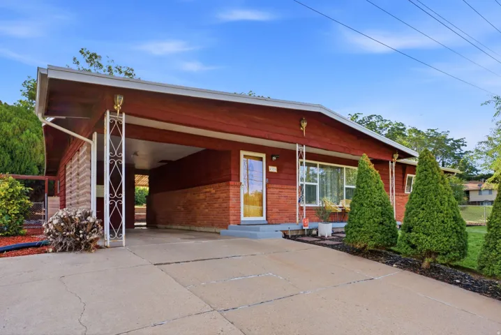 Red brick and wood-paneled exterior, featuring an attached carport with decorative columns, a concrete driveway, and mature landscaping
