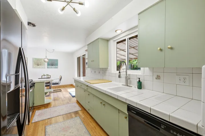 Kitchen featuring light green cabinetry, white tiled countertops, white tiled backsplash, a double basin sink, and wood-finish flooring