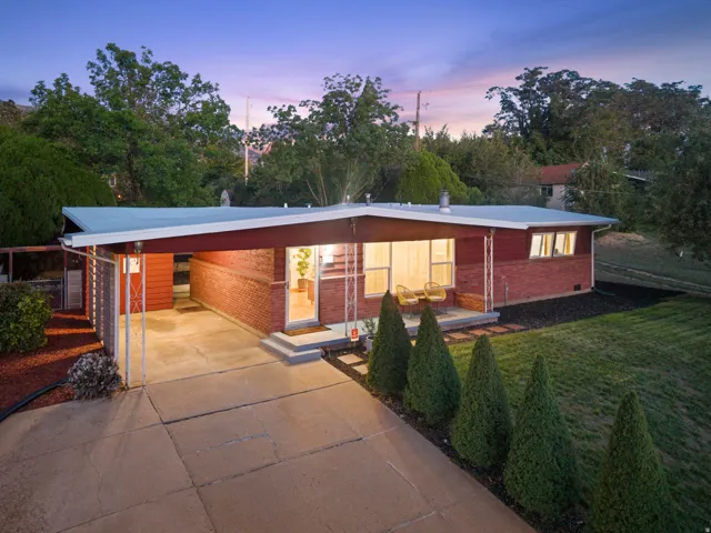 Mid-century modern residence featuring a brick facade, covered carport, concrete driveway, and established front landscaping